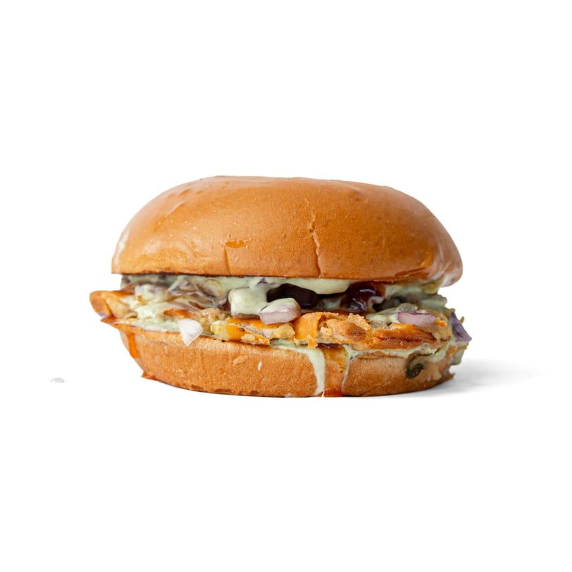 A close-up of a burger with chicken, cheese, onions, and green sauce on a white background.