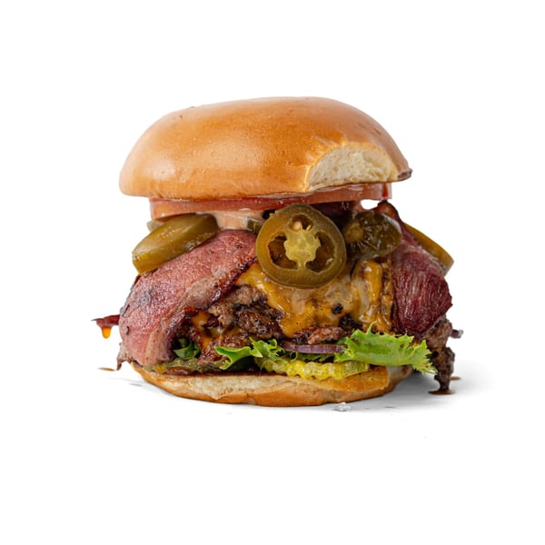 A large burger with beef patties, cheese, bacon, lettuce, pickles, and jalapenos on a bun.