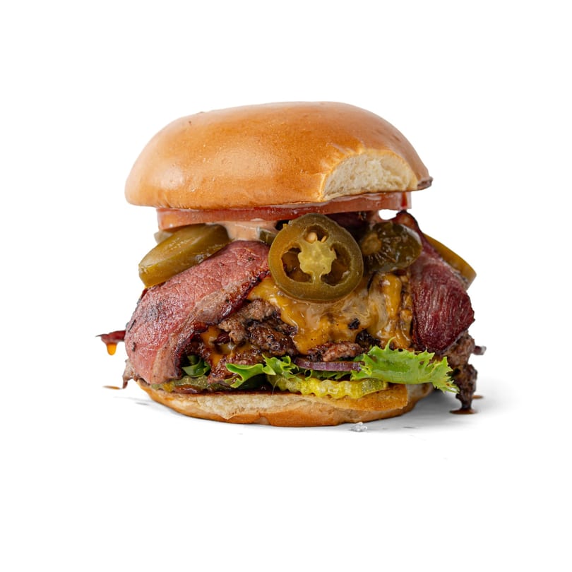 A large burger with beef patties, cheese, bacon, lettuce, pickles, and jalapenos on a bun.
