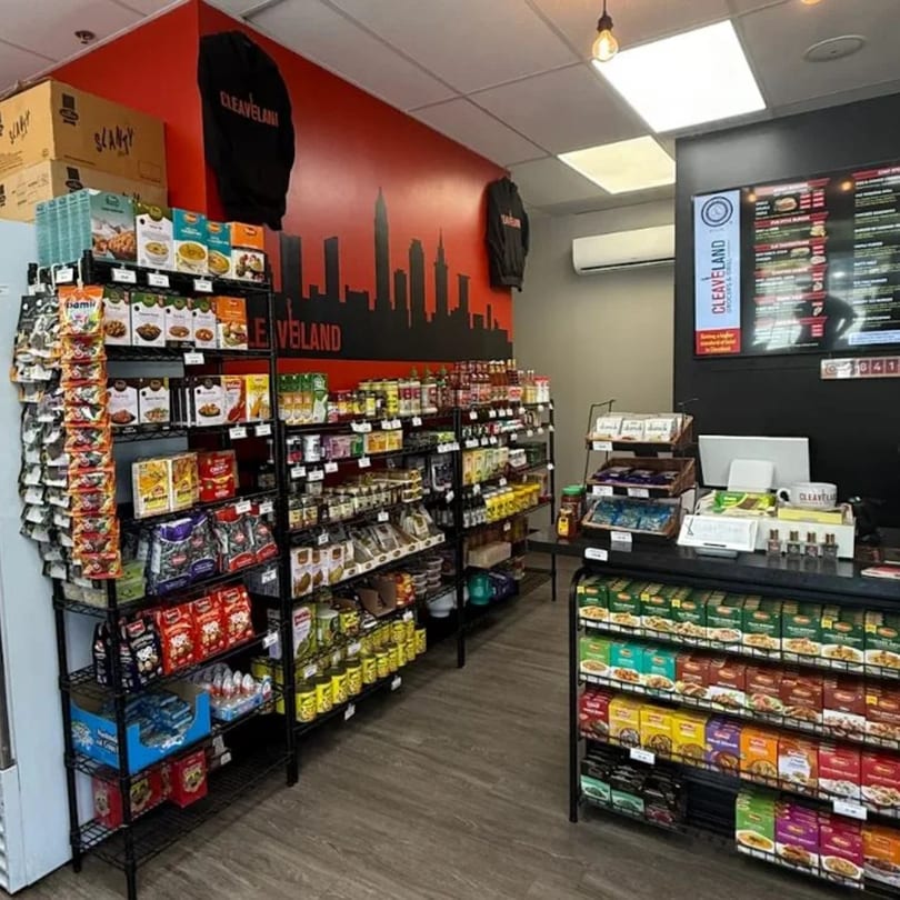 Interior of Cleaveland Grocers & Grill, showcasing shelves stocked with diverse food products and a menu board.