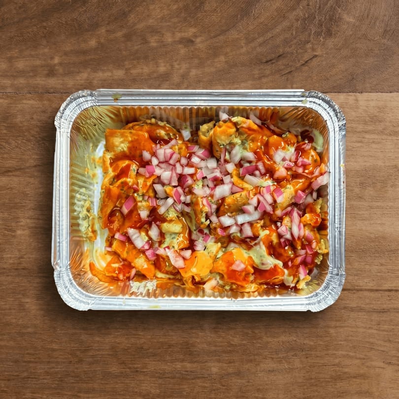 Top-down view of a foil container filled with saucy food topped with diced red onions.